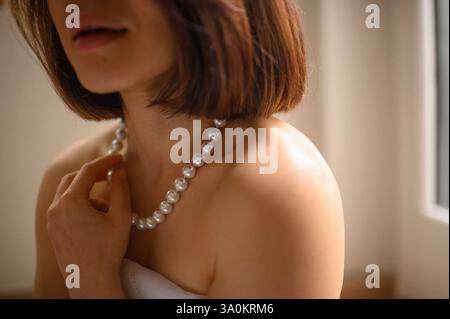 Une jeune femme regarde doucement, portant une élégante boucle d'oreille en perles et un collier assorti. Banque D'Images
