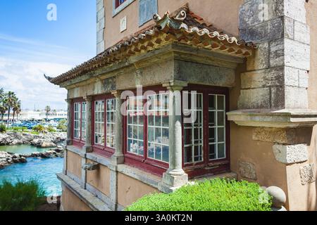 Gros plan sur un coin d'un charmant bâtiment avec des détails architecturaux traditionnels, avec de grandes fenêtres à cadre rouge, des colonnes de pierre et un toit carrelé Banque D'Images