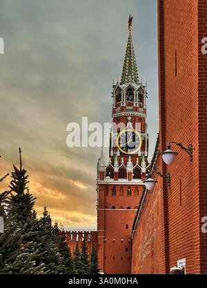 Majestueuse tour de l'horloge s'élève contre un ciel de coucher de soleil vibrant près de murs de briques rouges ornés d'arbres d'hiver à Moscou Banque D'Images