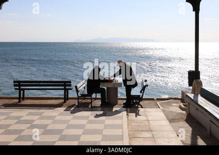 Athènes, Grèce - 4 mars 2025. Silhouettes de deux hommes âgés jouant aux échecs au bord de la mer Banque D'Images