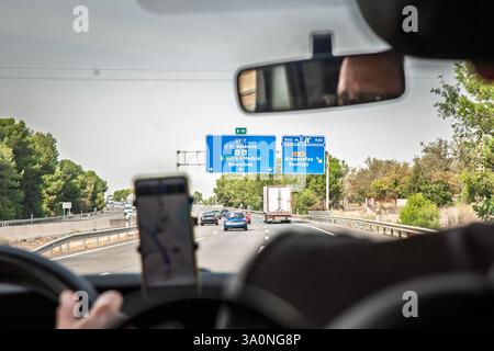 VALENCE, ESPAGNE - 13 OCTOBRE 2024 : un panneau autoroutier espagnol indique les routes vers Valence, Barcelone et Madrid. Les voitures roulent le long de l'autoroute, réfléchissent Banque D'Images