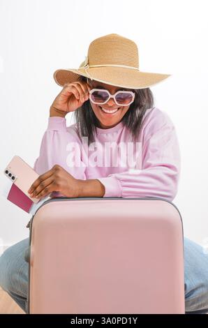 Jeune femme noire avec chapeau de soleil et lunettes de soleil tenant passeport et smartphone est prête pour les vacances d'été Banque D'Images