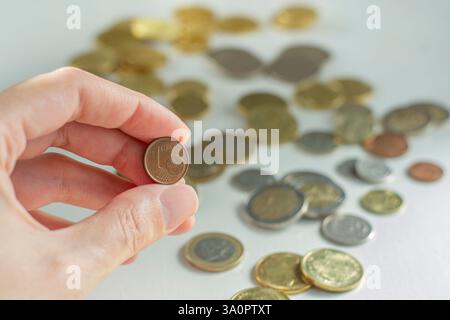 Main tenant une pièce de 1 centime d'euro devant de nombreuses pièces en arrière-plan Banque D'Images