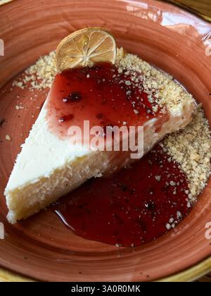 Gros plan d'une tranche de cheesecake garnie de sauce aux baies, de noix écrasées et d'une garniture de citron séchée, servie dans un plat en céramique. L'image est adaptée à Banque D'Images