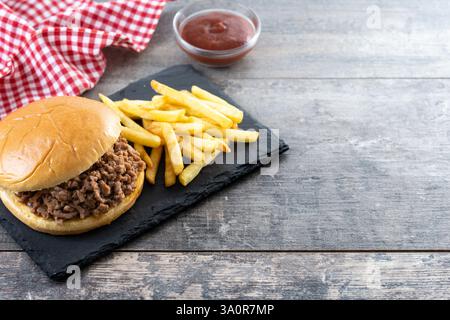 Sandwich traditionnel Sloppy joe avec frites sur table en bois et fond noir Banque D'Images