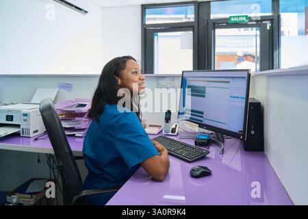 Réceptionniste noire souriante travaillant à son bureau dans une clinique dentaire moderne, utilisant un logiciel informatique pour gérer les données des patients et les rendez-vous Banque D'Images