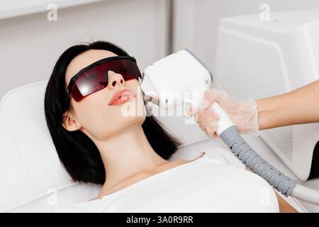 Thérapeute-cosmétologue effectue un traitement au laser sur le visage d'une femme dans une clinique de spa de beauté. Gros plan. Le concept de publicité saine Banque D'Images