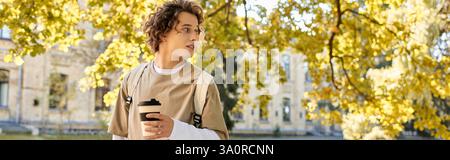 Un jeune homme élégant marche à travers un paysage d'automne coloré avec une tasse à café. Banque D'Images
