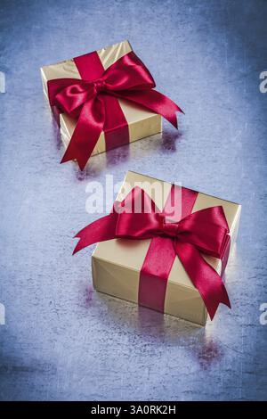 Cadeaux dorés en boîte avec noeud rouge sur fond métallique rayé Banque D'Images