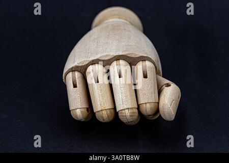 Une main de marionnette en bois montrant un poing, l'idée de ​​making un geste de puissance ou de salutation sur un fond noir. Banque D'Images