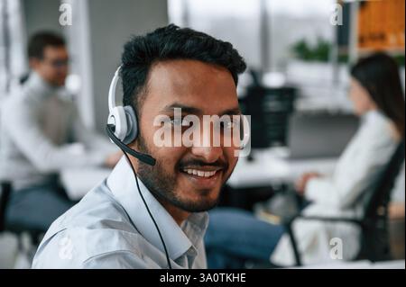 Portrait de Guy dans les écouteurs. Les hommes et les femmes travaillent ensemble au bureau. Banque D'Images