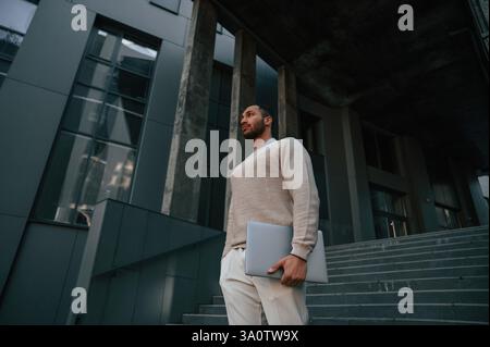 Positif bel homme noir est à l'extérieur près du bâtiment d'affaires tenant l'ordinateur portable. Banque D'Images
