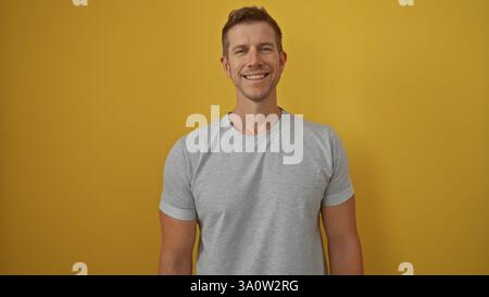 Jeune homme souriant avec confiance sur un fond jaune vif présentant un portrait attrayant et décontracté idéal pour le marketing moderne et lifestyl Banque D'Images
