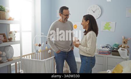 Couple hispanique d'âge moyen dans une chambre confortable partage un moment tendre, femme tenant le café, entouré par un décor chaleureux et des éléments de chambre de bébé, incarnant l Banque D'Images