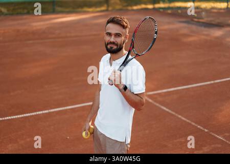 Jeune homme positif est sur le court de tennis à la journée ensoleillée. raquette de retenue. Banque D'Images