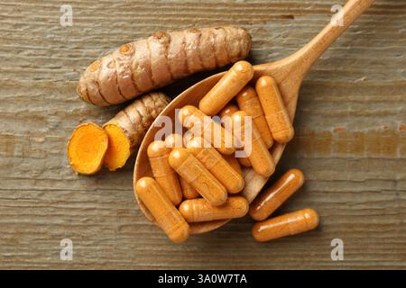Capsules de curcuma en cuillère et racines sur table en bois, pose à plat Banque D'Images