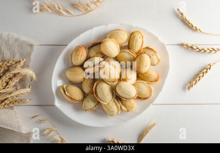 Délicieux biscuits sous la forme d'une noix remplie de lait condensé bouilli sur un fond en bois blanc, plat. Banque D'Images