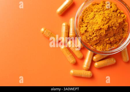 Poudre de curcuma dans un bol et capsules sur fond orange, plat. Espace pour le texte Banque D'Images