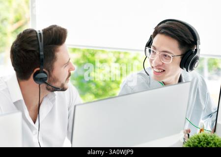 Les opérateurs de service d'assistance à la clientèle masculins équipés de micro-casques/oreillettes parlent à la lumière bureau Banque D'Images