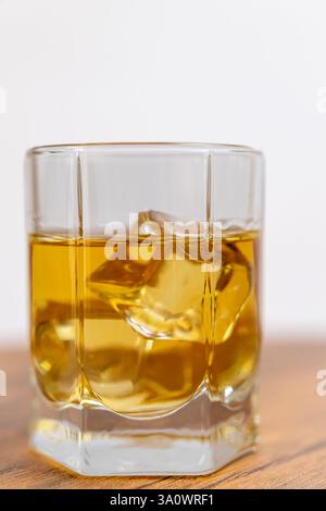 Gros plan d'un verre de whisky sur les rochers, reposant sur une surface en bois, avec un fond blanc flou Banque D'Images