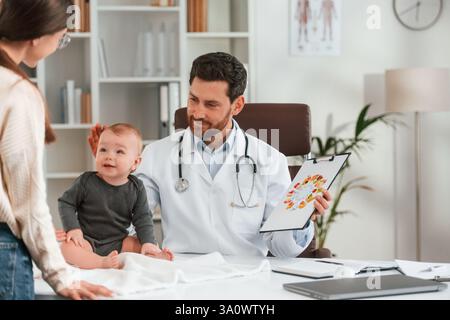 Parler d'une alimentation saine. Avec bébé et mère. Docteur en vêtements formels travaille dans le cabinet. Banque D'Images