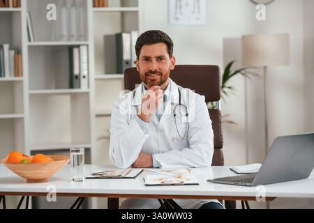 En manteau blanc, assis. Docteur en vêtements formels travaille dans le cabinet. Banque D'Images