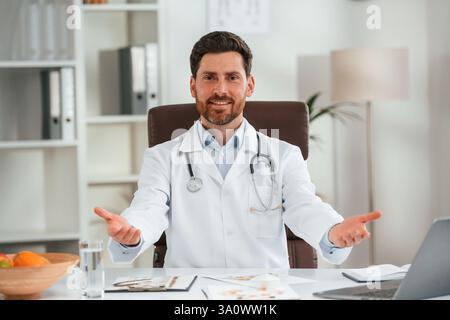 En manteau blanc, assis. Docteur en vêtements formels travaille dans le cabinet. Banque D'Images