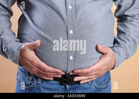 Homme en surpoids dans une chemise serrée sur fond beige, gros plan Banque D'Images