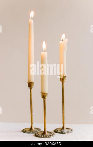 Trois grandes bougies blanches brillent sur les bougeoirs en laiton ornés, créant une ambiance chaleureuse et accueillante. Banque D'Images