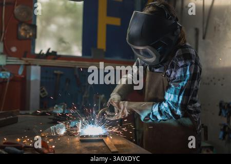 Habile et dévoué soudeur femelle soudeur en acier dans un atelier à la maison sombre. Concept de démarrage de petite entreprise. Banque D'Images