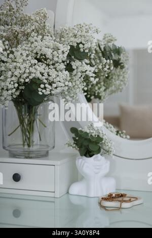 Bouquet de belles fleurs de gypsophila et branches d'eucalyptus dans un vase sur une coiffeuse près du miroir à l'intérieur Banque D'Images
