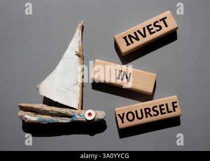 Investissez dans vous symbole. Mots conceptuels investissez en vous-même sur des blocs de bois. Beau fond gris avec bateau. Affaires et investir dans vous con Banque D'Images