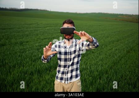 Lunettes de réalité virtuelle noires. Jouer à un jeu. Beau jeune homme est dans un champ agricole. Banque D'Images