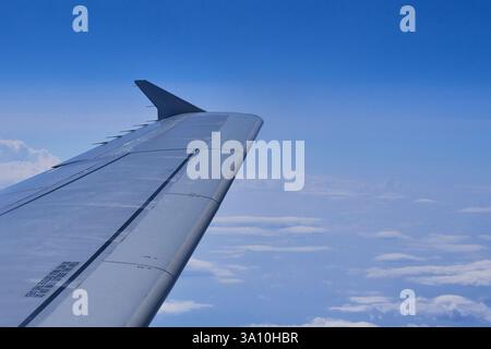 Vue d'une fenêtre d'avion montrant l'aile et l'ailette volant au-dessus d'une couverture de nuages blancs sous un ciel bleu clair Banque D'Images