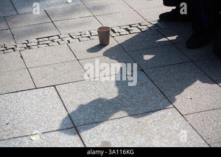 Berlin, Allemagne. 10 juillet 2023. L'ombre d'une personne avec une tasse pour les dons tombe sur le trottoir. Crédit : Fernando Gutierrez-Juarez/dpa/Alamy Live News Banque D'Images