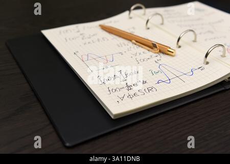 Un carnet ouvert révèle des équations mathématiques complexes et des graphiques colorés, accompagnés d'un luxueux stylo doré Banque D'Images