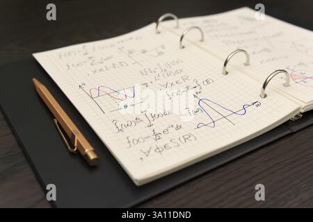 Un carnet ouvert révèle des équations mathématiques complexes et des graphiques colorés, accompagnés d'un luxueux stylo doré Banque D'Images
