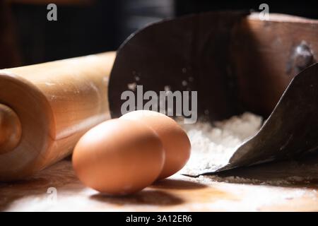 Cette installation de cuisson rustique comprend de la pâte maison, des œufs, de la farine et un rouleau à pâtisserie en bois. Amateurs de pâtisserie à la recherche d'une scène de cuisine de ferme. Banque D'Images