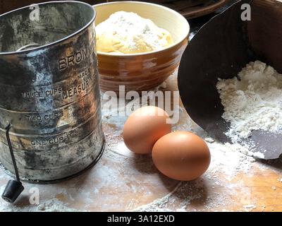 Cette installation de cuisson rustique comprend de la pâte maison, des œufs, de la farine et un rouleau à pâtisserie en bois. Amateurs de pâtisserie à la recherche d'une scène de cuisine de ferme. Banque D'Images