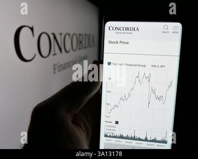 Dans cette illustration photo, une personne tient un téléphone portable avec la page Web de la société japonaise Concordia Financial Group Ltd sur l'écran avec logo. Banque D'Images