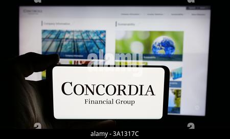 Dans cette illustration photo, une personne tient un téléphone cellulaire avec le logo de la société japonaise Concordia Financial Group Ltd sur l'écran devant la page Web. Banque D'Images