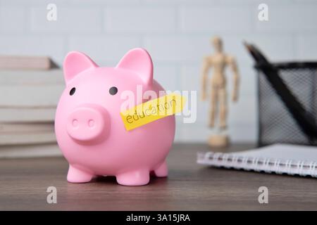 Une tirelire rose avec une note collante jaune étiquetée «éducation» attachée à son côté. Concept d'épargne pour l'éducation. Banque D'Images