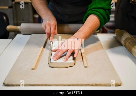 Artisan travaillant sur le projet de poterie, coupant la dalle d'argile à l'aide d'un couteau et de guides en bois Banque D'Images