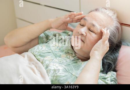 Plan recadré d'une femme âgée fatiguée souffrant de maux de tête ou de migraine, se sentant mal, souffrant d'insomnie dans la chambre. Banque D'Images