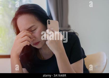 La femme asiatique adulte bouleversée avec le téléphone intelligent ressent la tristesse solitaire souffrant de mauvaise relation. Espace de copie, mise au point sélective. Banque D'Images