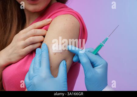 Gros plan d’un professionnel de santé appliquant un bandage après une vaccination, avec une seringue à la main, assurant les soins post-injection et la sécurité du patient. Banque D'Images