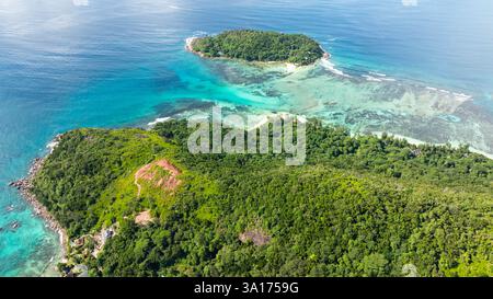 Une petite île couverte d'une végétation dense, entourée d'eaux turquoises claires et de récifs coralliens. Praslin, îles rondes. Seychelles. Banque D'Images
