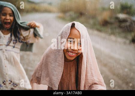 Filles noires souriantes dansant sous la pluie dans la campagne Banque D'Images