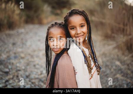 Sœurs noires filles de race mixte souriantes dans les champs avec des rochers Banque D'Images