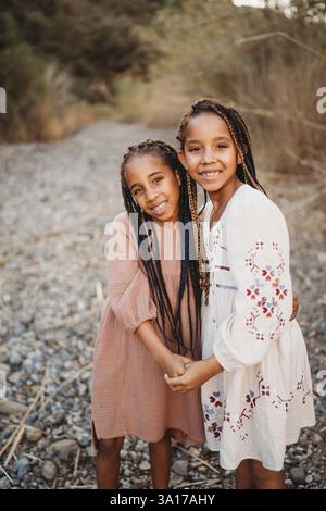 Sœurs noires filles de race mixte souriantes dans les champs avec des rochers Banque D'Images